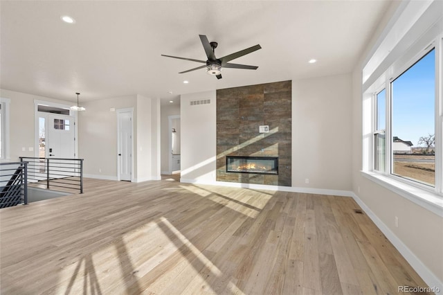 unfurnished living room featuring a tiled fireplace, light hardwood / wood-style flooring, and ceiling fan