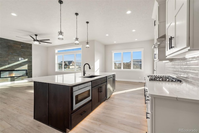 kitchen featuring sink, hanging light fixtures, an island with sink, stainless steel appliances, and white cabinets