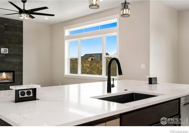 kitchen featuring pendant lighting, a large fireplace, sink, and light stone counters