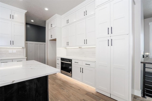 kitchen with light hardwood / wood-style flooring, light stone counters, white cabinets, a textured ceiling, and stainless steel oven