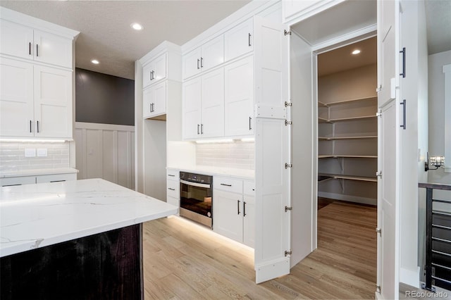 kitchen with light hardwood / wood-style flooring, oven, white cabinets, light stone countertops, and backsplash