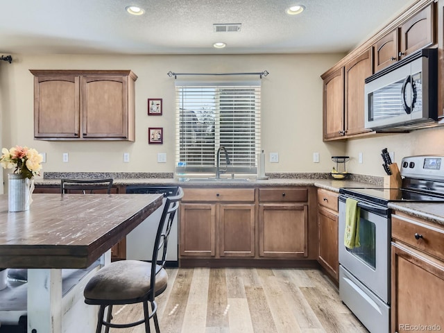 kitchen with stainless steel appliances, light hardwood / wood-style floors, a textured ceiling, and sink