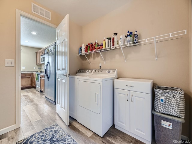 clothes washing area with a textured ceiling, light hardwood / wood-style floors, washer and dryer, and cabinets