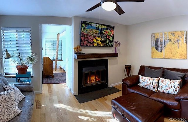 living room featuring ceiling fan, wood finished floors, a fireplace with flush hearth, and baseboards