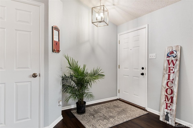 entrance foyer with a textured ceiling, baseboards, an inviting chandelier, and dark wood-style floors