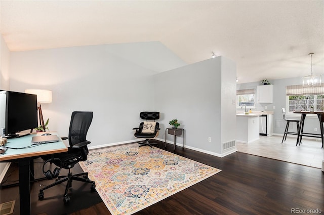 home office featuring visible vents, wood finished floors, baseboards, a sink, and vaulted ceiling