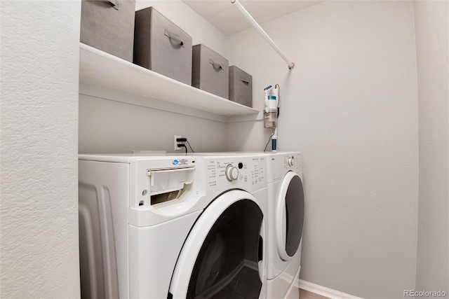 washroom featuring laundry area, baseboards, a textured wall, and separate washer and dryer