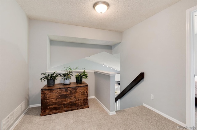 stairway with carpet flooring, a textured ceiling, and visible vents