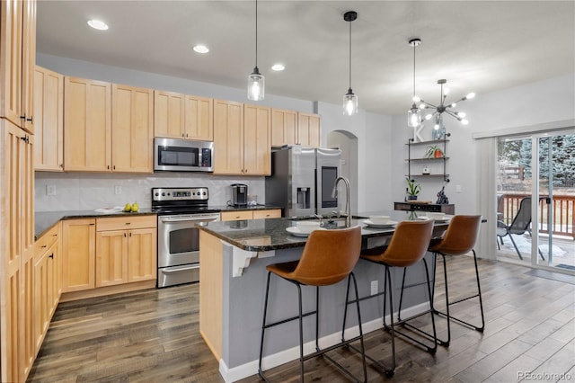 kitchen with appliances with stainless steel finishes, a center island with sink, dark hardwood / wood-style floors, and light brown cabinetry