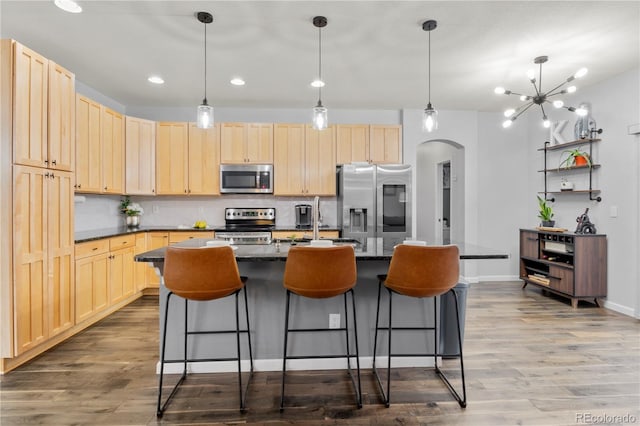 kitchen featuring a center island with sink, decorative light fixtures, wood-type flooring, and appliances with stainless steel finishes