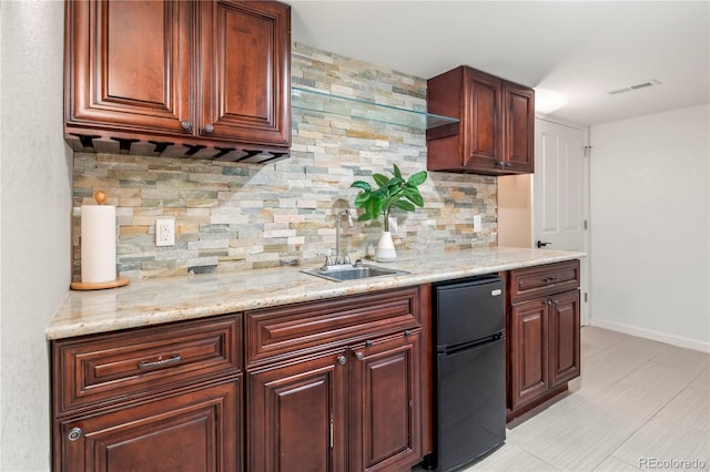 kitchen featuring decorative backsplash, light stone counters, black fridge, sink, and light tile patterned floors