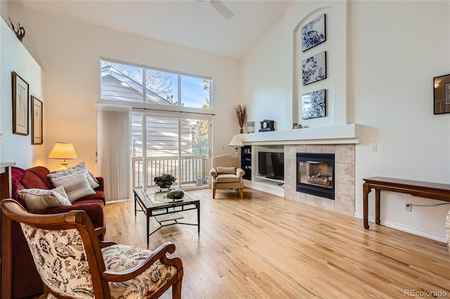 interior space featuring a tiled fireplace, ceiling fan, high vaulted ceiling, and light wood-type flooring