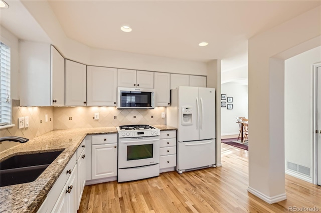 kitchen with white appliances, sink, light stone countertops, light wood-type flooring, and white cabinetry