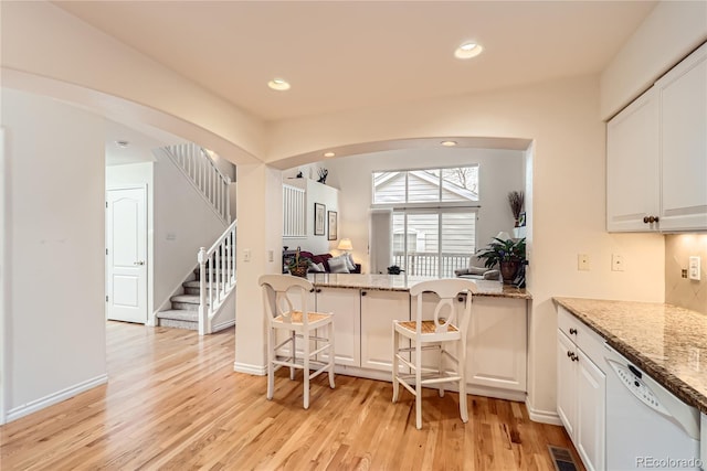 kitchen with light stone counters, kitchen peninsula, white dishwasher, light hardwood / wood-style floors, and white cabinets