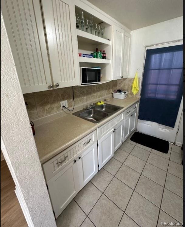 kitchen with backsplash, sink, light tile floors, and white cabinets