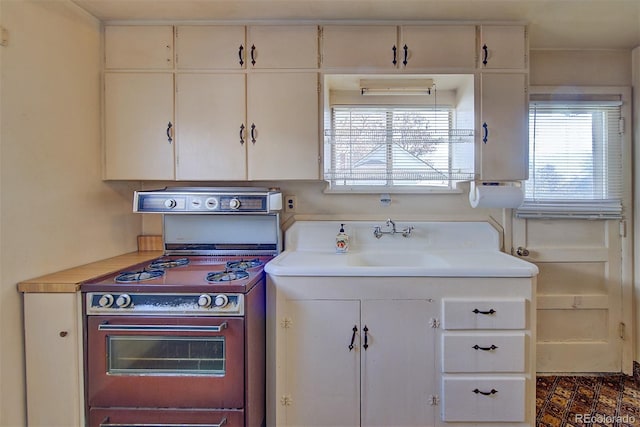 kitchen featuring stove, white cabinetry, and sink