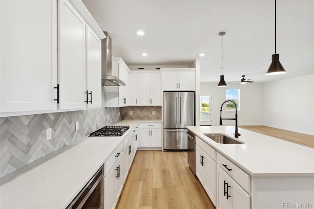 kitchen with a sink, backsplash, appliances with stainless steel finishes, wall chimney exhaust hood, and light countertops