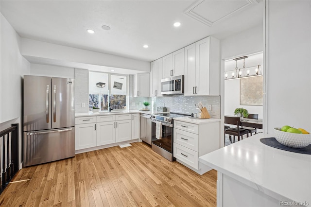 kitchen featuring backsplash, light wood-type flooring, white cabinets, and appliances with stainless steel finishes