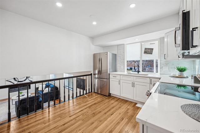 kitchen featuring white cabinetry, sink, backsplash, light hardwood / wood-style floors, and stainless steel appliances