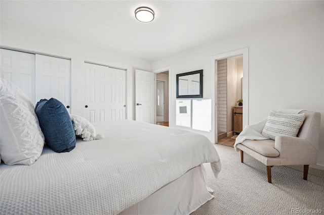 carpeted bedroom featuring connected bathroom and two closets