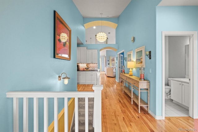 hallway featuring arched walkways, light wood-type flooring, and a high ceiling