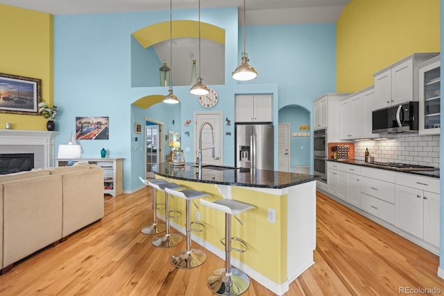 kitchen featuring a breakfast bar, arched walkways, a sink, appliances with stainless steel finishes, and a glass covered fireplace