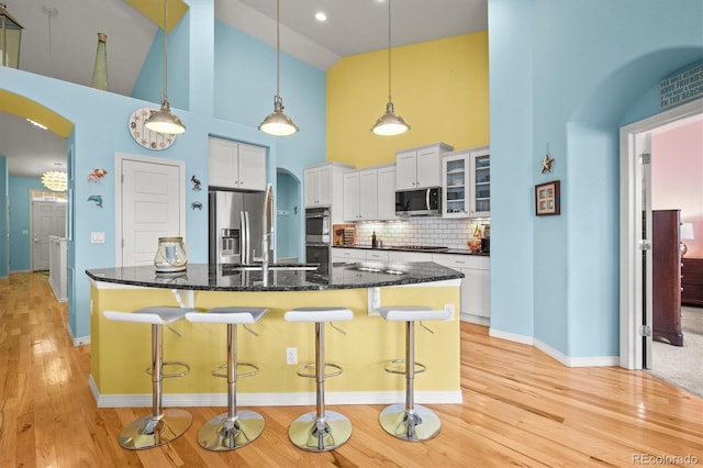 kitchen featuring a kitchen breakfast bar, tasteful backsplash, stainless steel appliances, arched walkways, and white cabinets