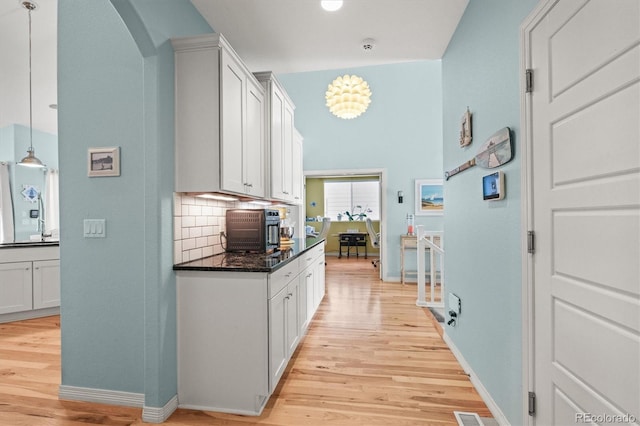 kitchen with arched walkways, tasteful backsplash, light wood-style flooring, and white cabinets