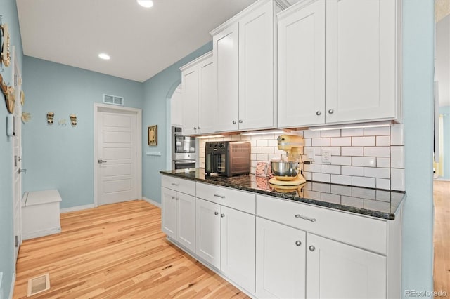 kitchen with visible vents, backsplash, dark stone counters, white cabinets, and light wood finished floors