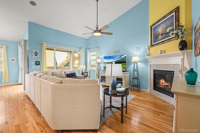 living room with light wood-type flooring, high vaulted ceiling, a ceiling fan, baseboards, and a tile fireplace