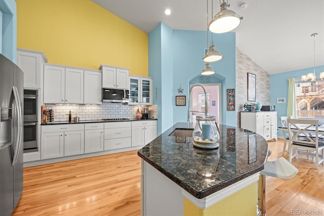 kitchen featuring light wood finished floors, tasteful backsplash, appliances with stainless steel finishes, hanging light fixtures, and white cabinetry