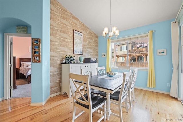 dining room featuring baseboards, lofted ceiling, light wood-style flooring, an accent wall, and a chandelier