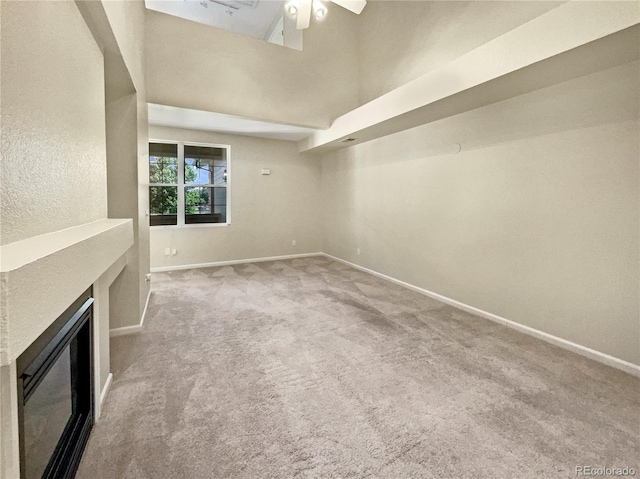 unfurnished living room with a fireplace, carpet flooring, a ceiling fan, a towering ceiling, and baseboards