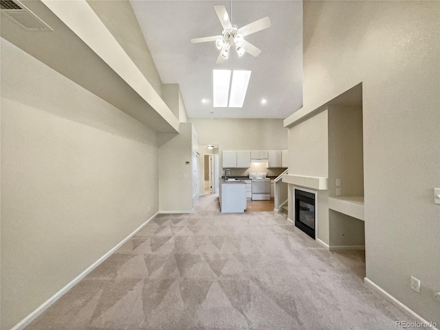 unfurnished living room featuring a skylight, sink, ceiling fan, a towering ceiling, and light carpet