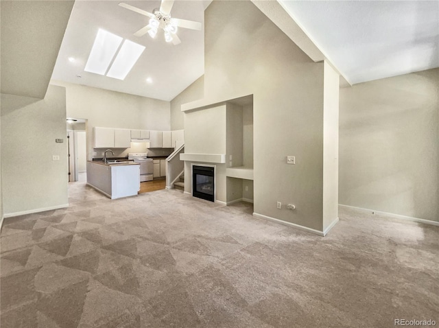 unfurnished living room with high vaulted ceiling, sink, a skylight, ceiling fan, and light colored carpet