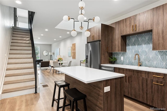 kitchen with stainless steel appliances, a sink, light countertops, a breakfast bar area, and decorative backsplash