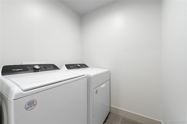 clothes washing area featuring washing machine and clothes dryer, tile patterned flooring, and baseboards