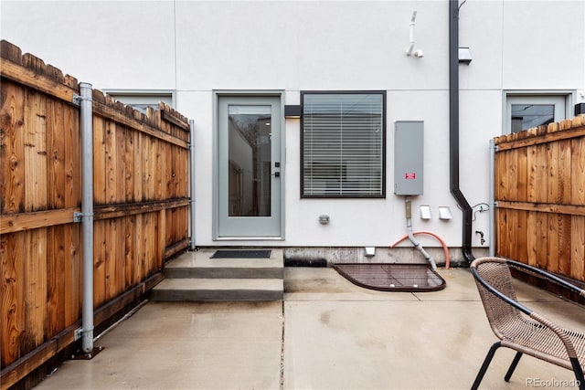 property entrance with fence, stucco siding, and a patio