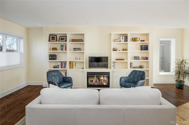 living area with dark wood-style floors, a glass covered fireplace, and baseboards