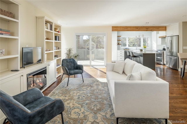 living area with dark wood finished floors, beamed ceiling, and a glass covered fireplace