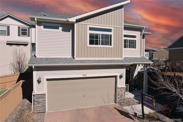 view of front of property featuring a garage, stone siding, roof with shingles, and fence