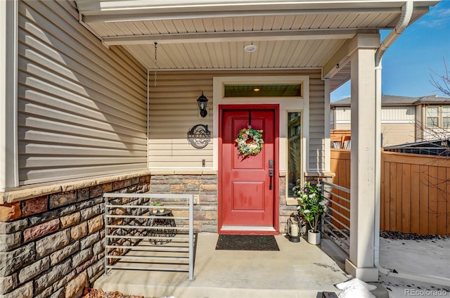 view of exterior entry with covered porch and fence