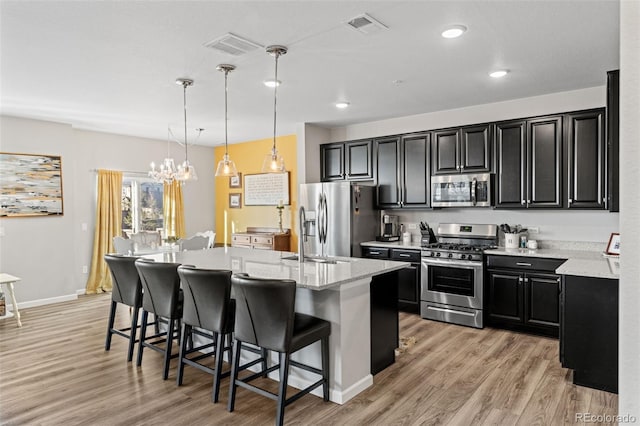 kitchen featuring pendant lighting, a kitchen island with sink, a breakfast bar area, light stone countertops, and stainless steel appliances