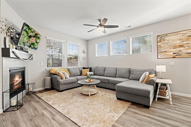 living room with a tiled fireplace, ceiling fan, and light wood-type flooring