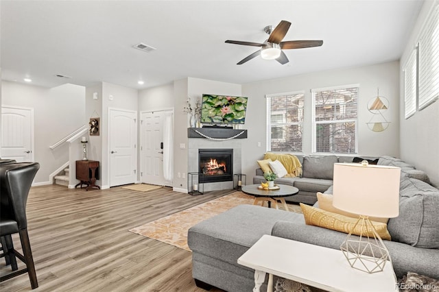 living room featuring a tiled fireplace, ceiling fan, and light wood-type flooring