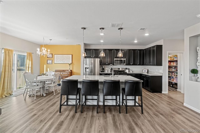 kitchen featuring a kitchen bar, appliances with stainless steel finishes, a kitchen island with sink, pendant lighting, and a chandelier