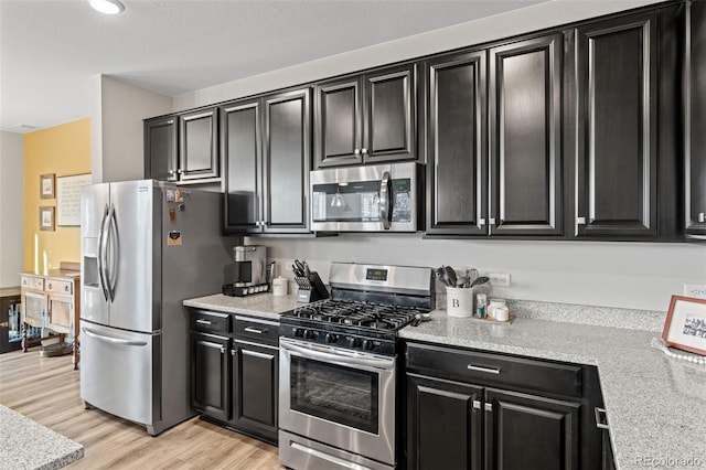 kitchen with light stone counters, stainless steel appliances, and light hardwood / wood-style flooring