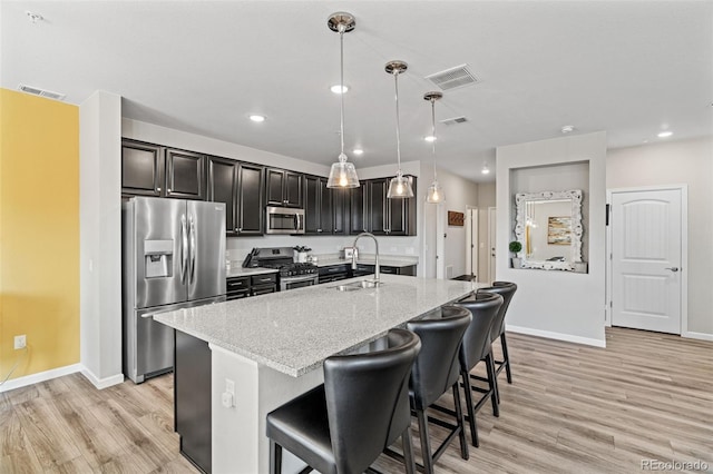 kitchen with light stone countertops, sink, pendant lighting, a kitchen island with sink, and appliances with stainless steel finishes