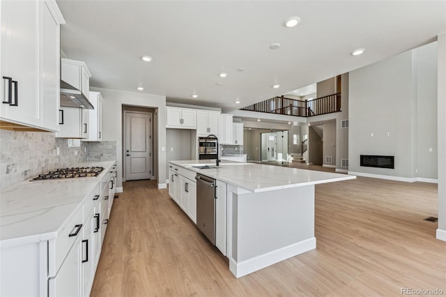 kitchen with light stone counters, white cabinets, appliances with stainless steel finishes, and a large island with sink