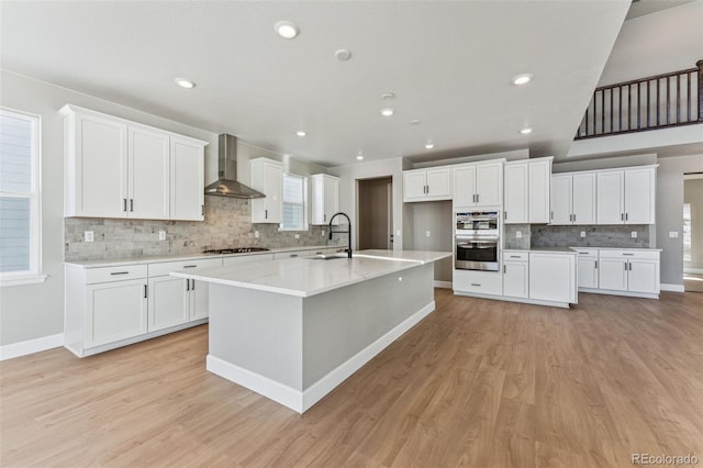 kitchen featuring a spacious island, wall chimney exhaust hood, white cabinetry, appliances with stainless steel finishes, and light stone countertops